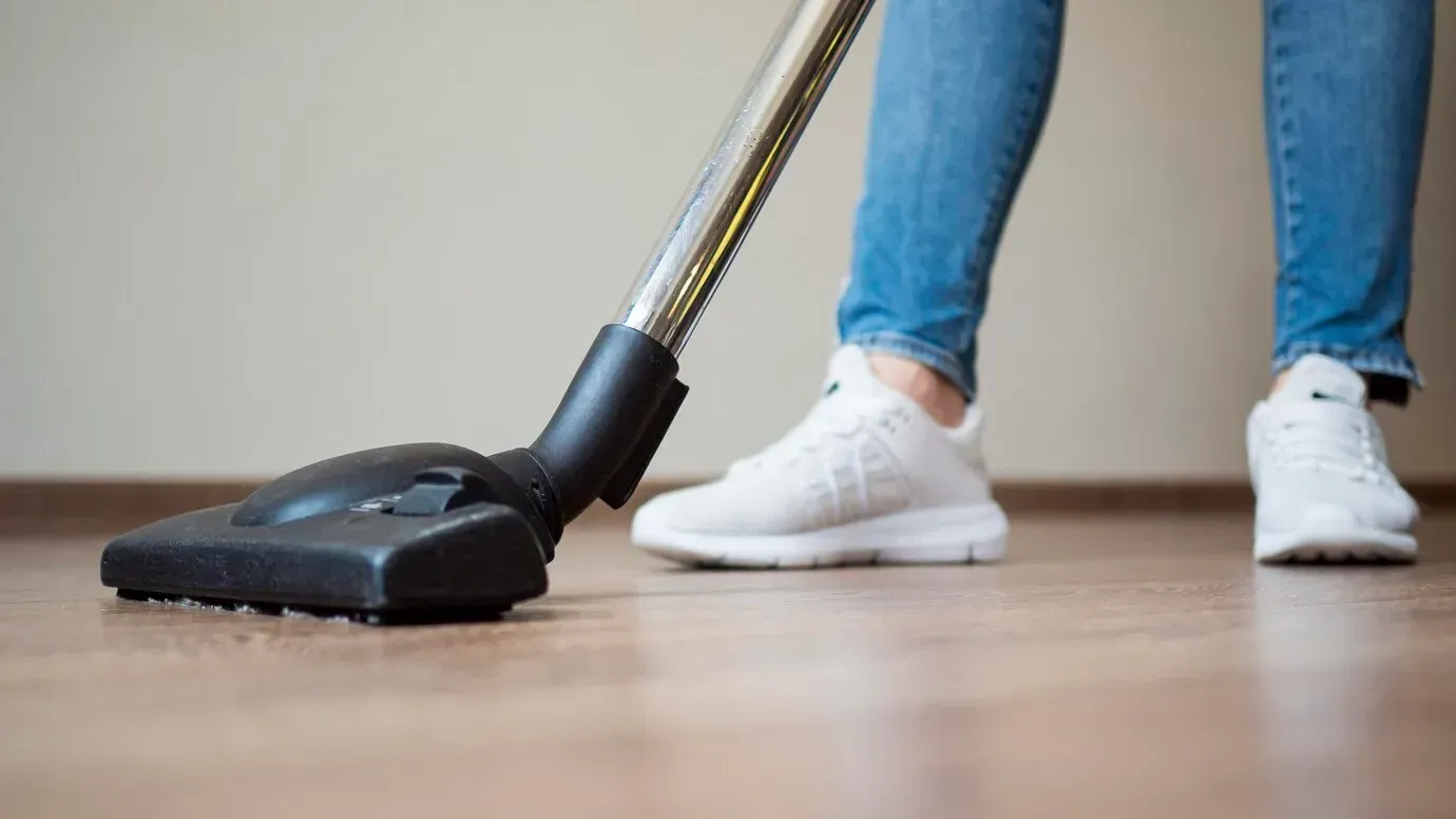 A person is using a vacuum cleaner on a wooden floor.