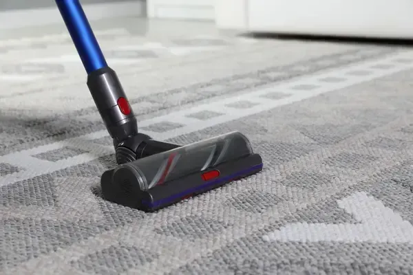 A vacuum cleaner is cleaning a carpet in a living room.