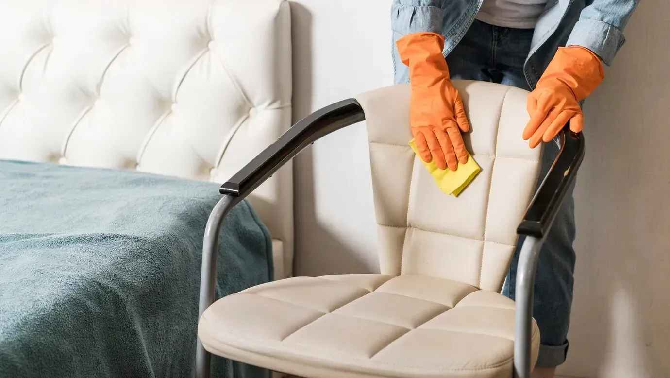 A woman is cleaning a chair with a sponge in a bedroom.