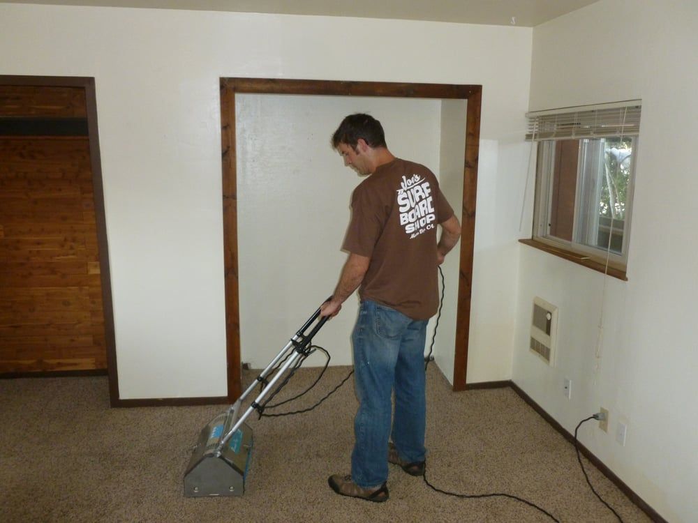 A man in a brown shirt is using a vacuum cleaner