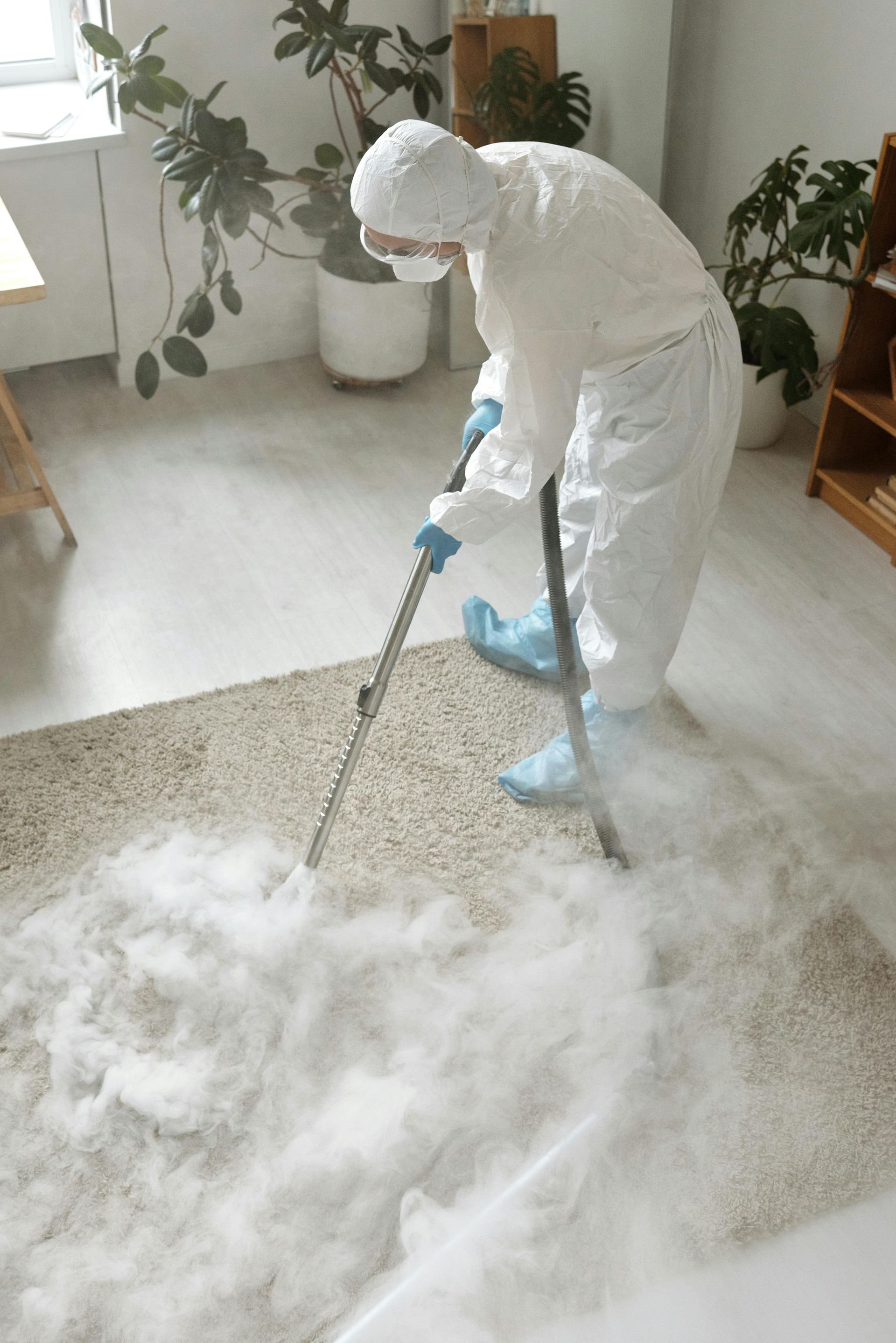 A man in a protective suit is cleaning a carpet with a vacuum cleaner.