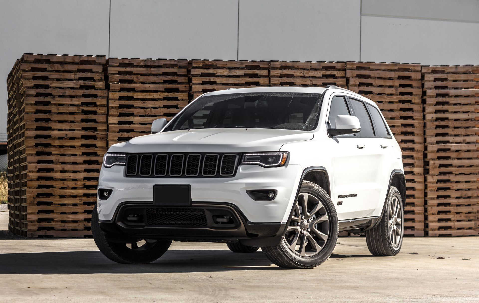 White Jeep Grand Cherokee SUV with black accents, parked in front of wood pallets.