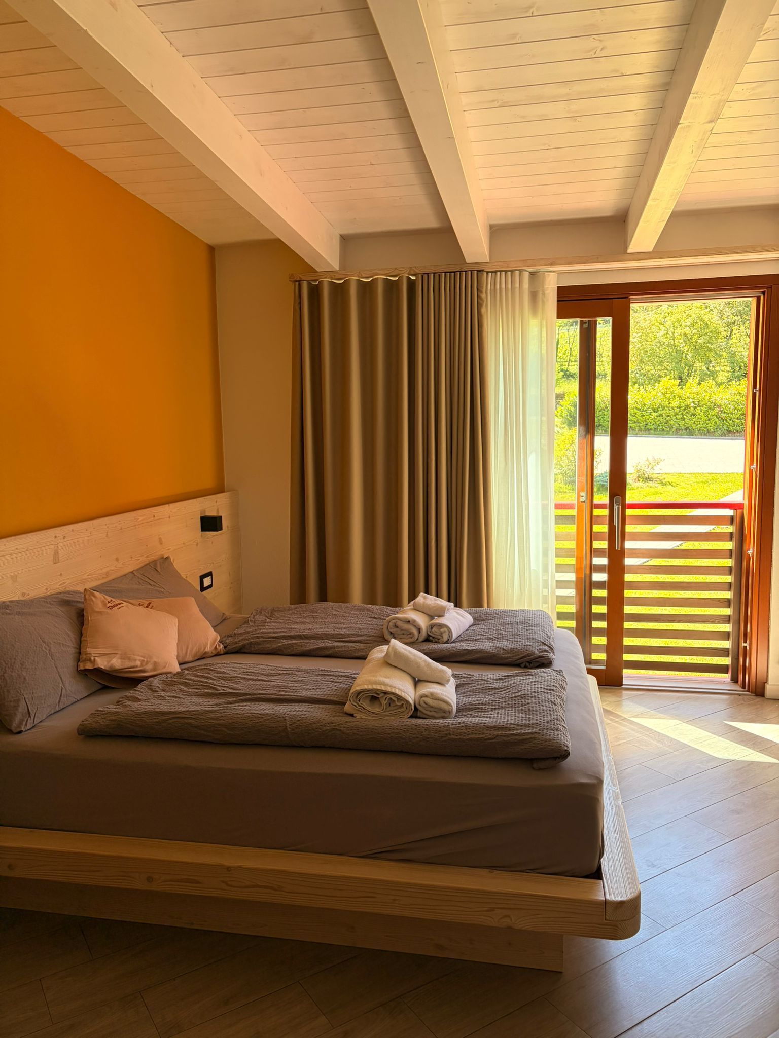 Camera da letto luminosa con due letti singoli, pareti color arancio caldo e porte finestre che si aprono sul verde.