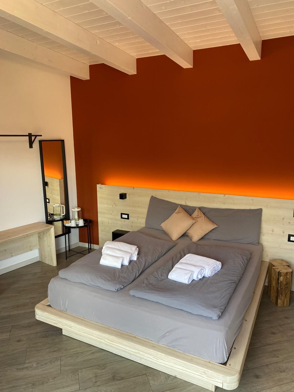 Camera da letto moderna con letto grigio, parete decorativa arancione e illuminazione calda sotto il letto.