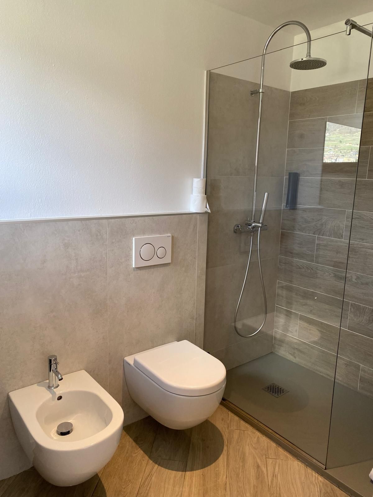 Bagno moderno con WC sospeso, bidet e box doccia in vetro nei toni del beige e del bianco.