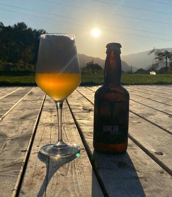 Un bicchiere e una bottiglia di birra su un tavolo di legno illuminato dal sole al tramonto, all'aperto.