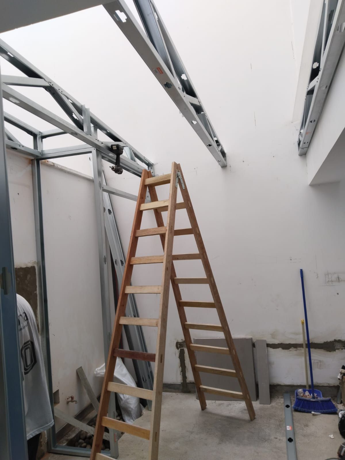 Escalera en una habitación blanca en construcción con la estructura del techo a la vista y herramientas en el suelo.