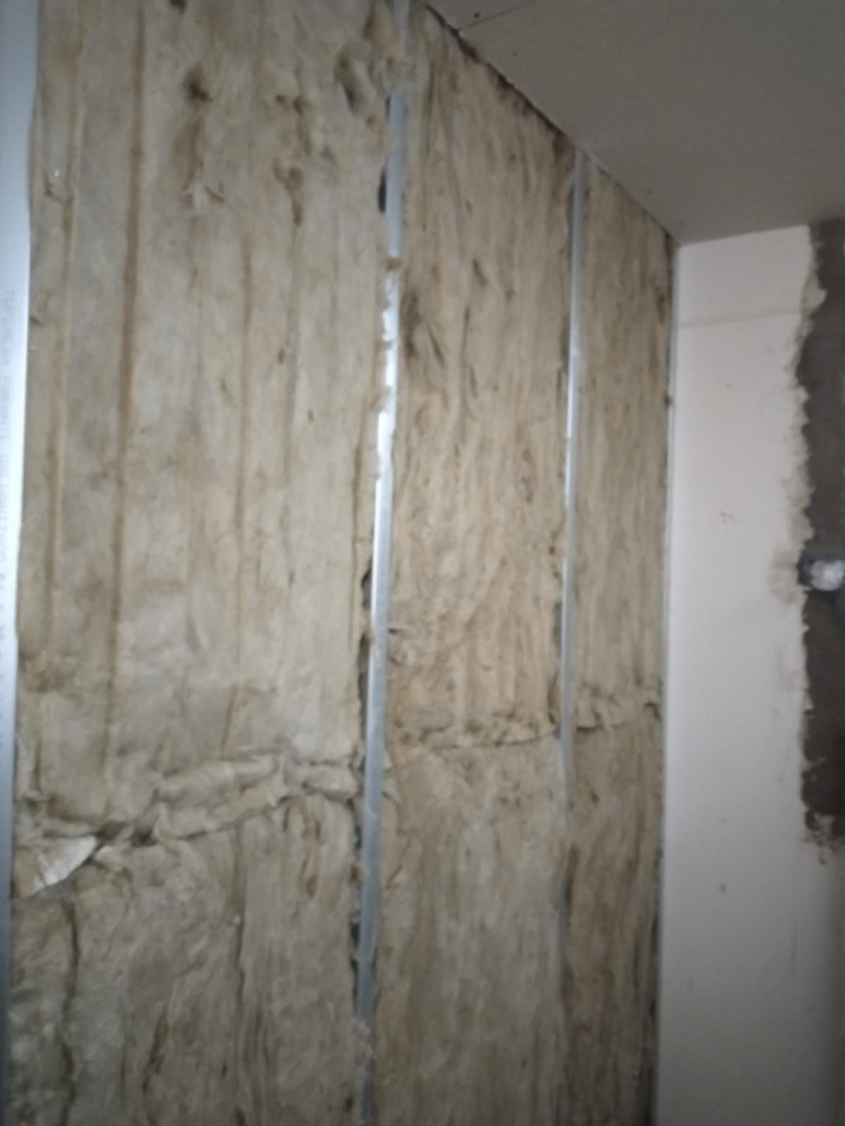 Pared sin terminar con aislamiento y juntas de paneles de yeso expuestas en una habitación en renovación.