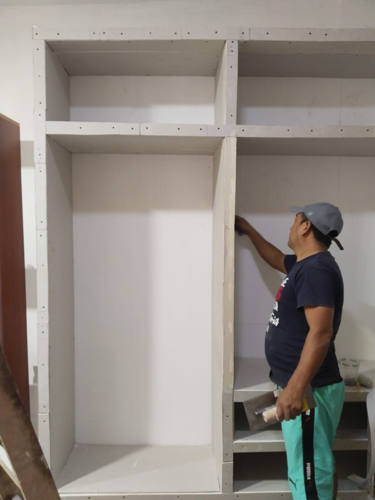 Hombre midiendo el marco de un armario empotrado con una cinta métrica en el interior de una vivienda.