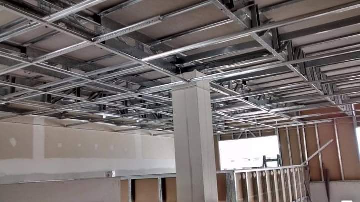 Obra en construcción con estructura de techo a la vista, conductos colgantes y paredes de pladur sin terminar.