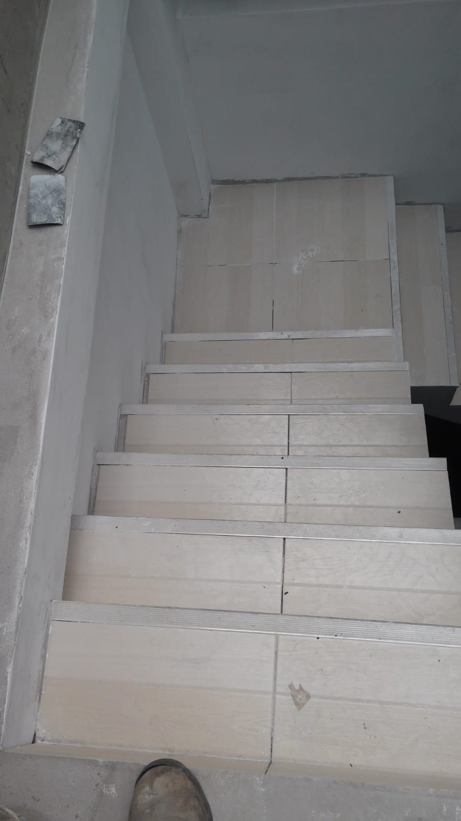 Estrecha escalera de hormigón sin terminar con escalones blancos que conducen hacia arriba y paredes grises.