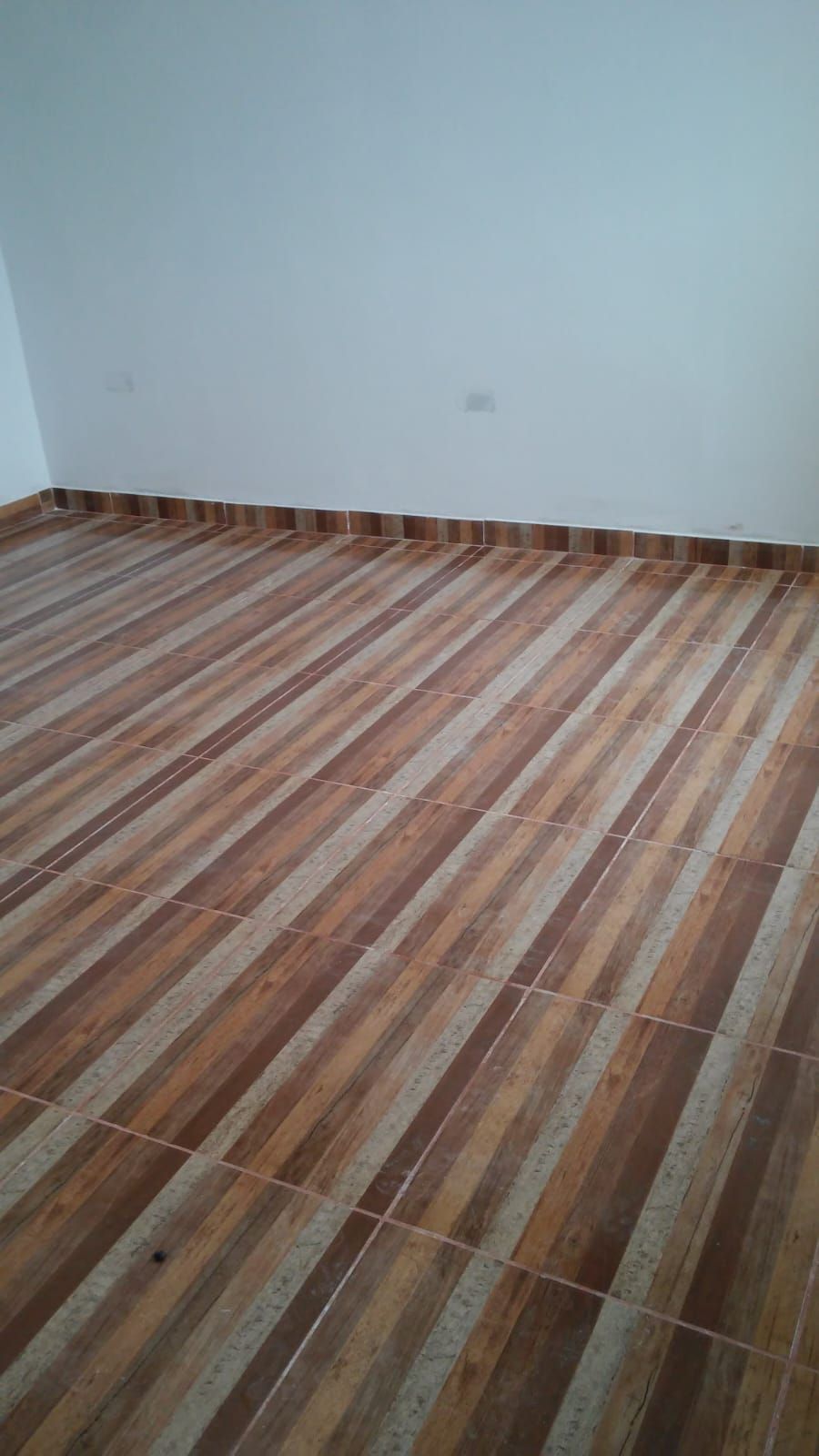 Habitación vacía con paredes blancas y suelo de baldosas marrones a rayas.