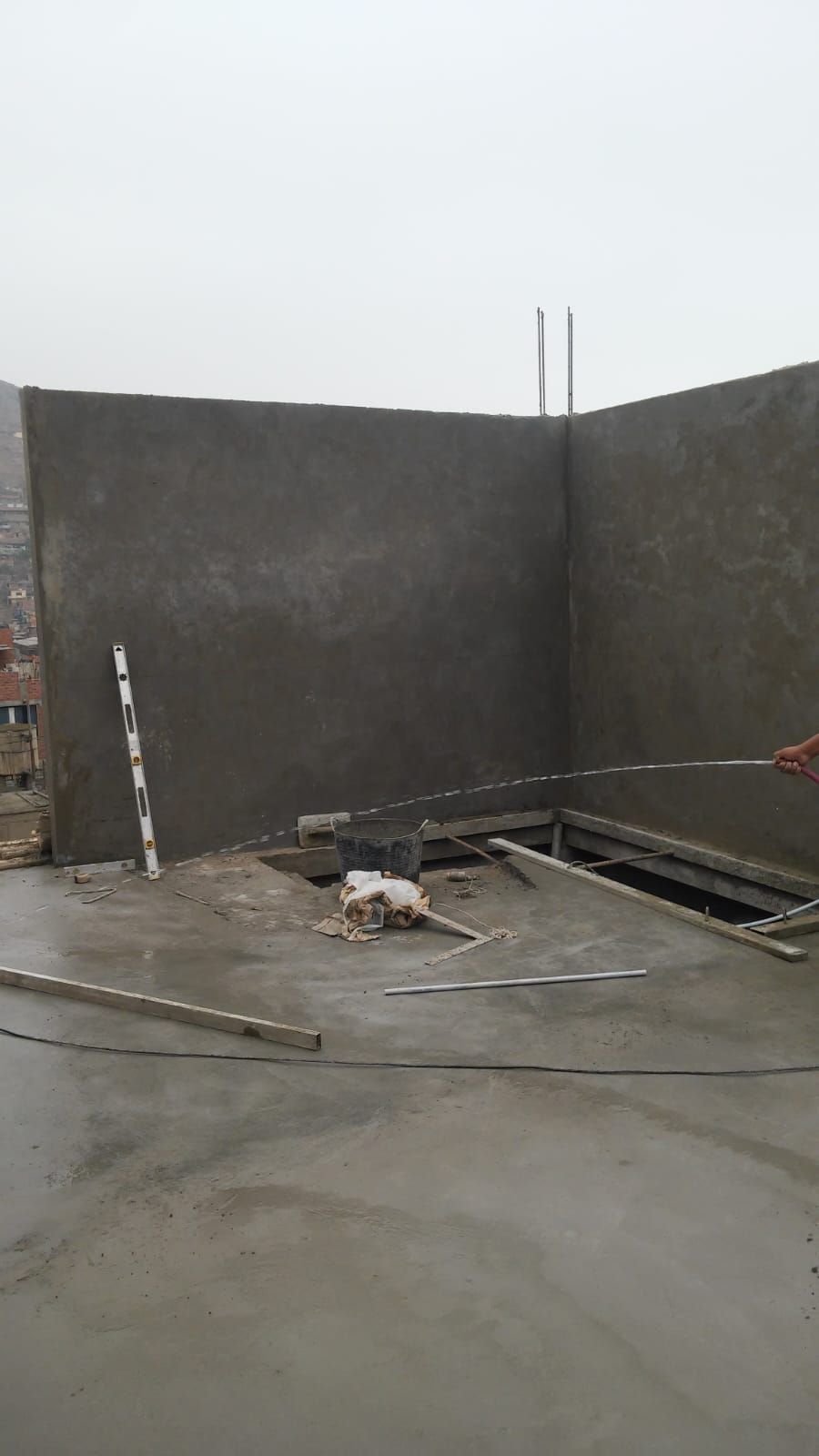 Obra en construcción de hormigón vacía con paredes grises sin terminar y escombros esparcidos por el suelo.