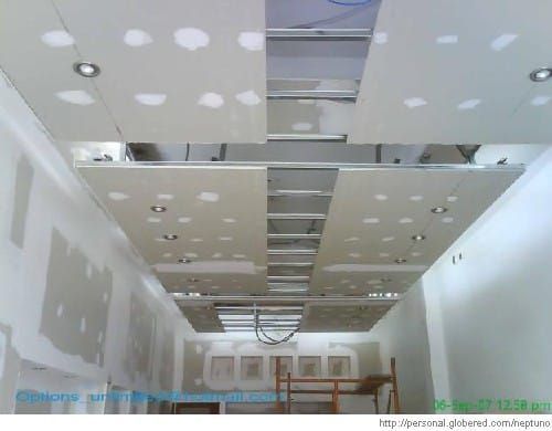 Pasillo largo y sin terminar con paneles de yeso en el techo, luces empotradas y conductos de ventilación a la vista.