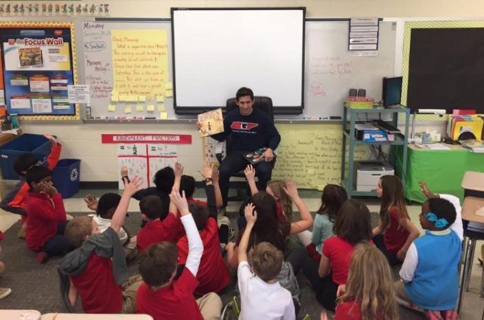 A man is reading a book to a group of children in a classroom