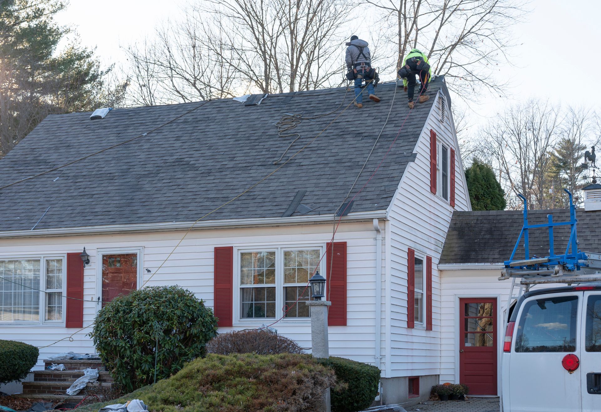 Workers on a white house roof installing or repairing shingles beside a ladder truck Workers on a white house roof installing or repairing shingles beside a ladder truck