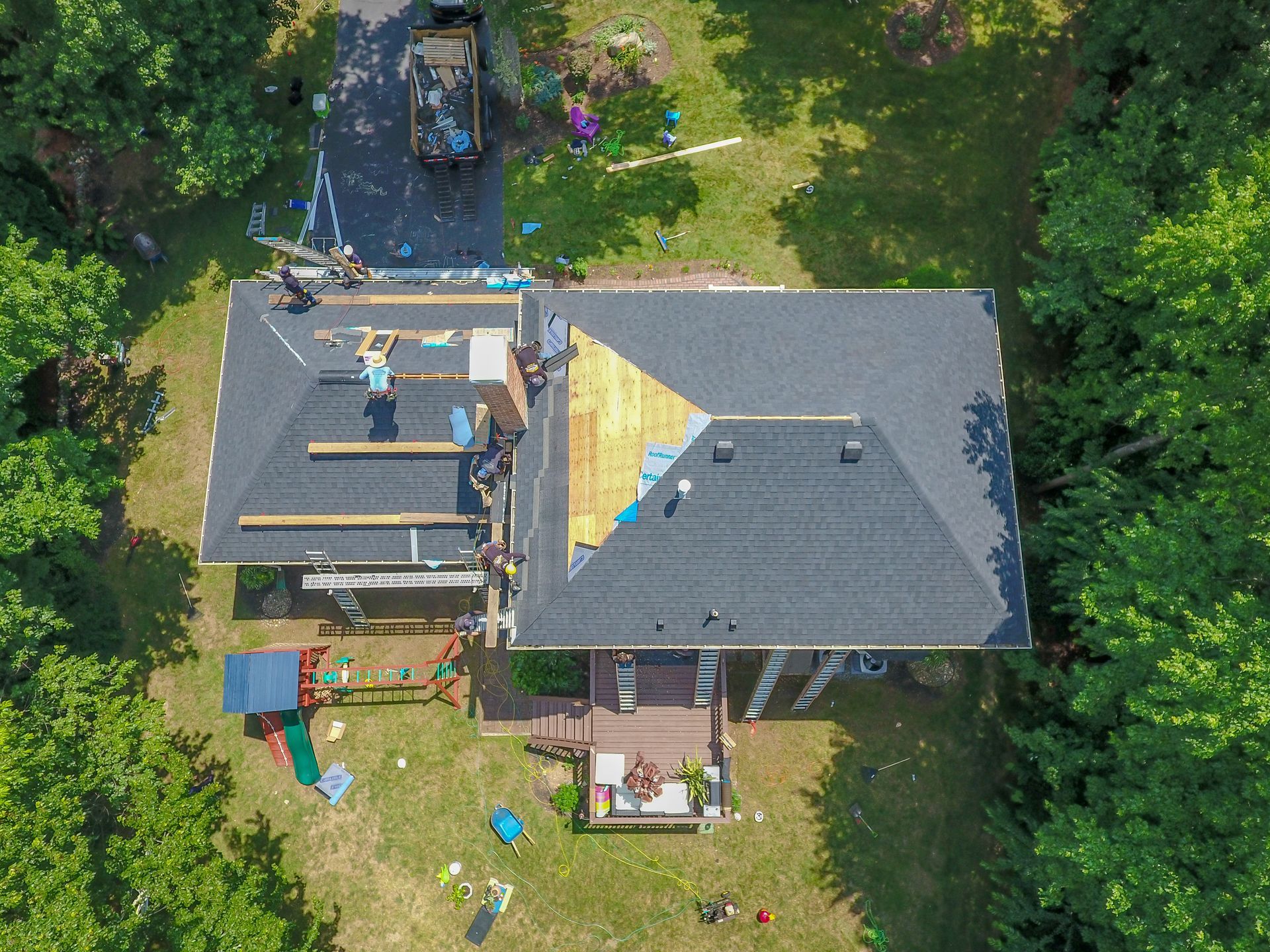 An aerial view of roofers replacing asphalt shingles on a residential home with exposed decking