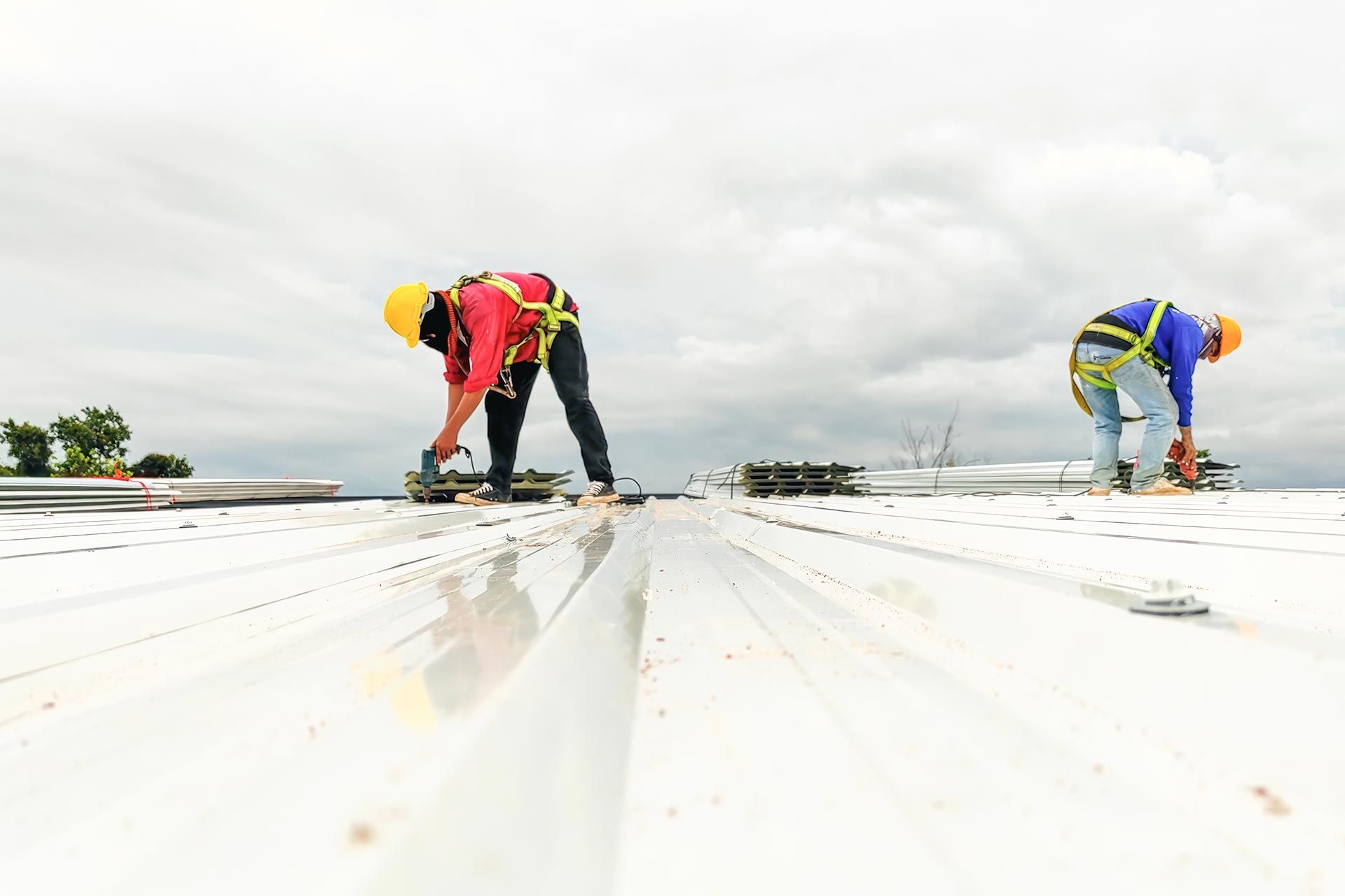 two construction workers installing or repairing a reflective white rooftop under a cloudy sky.