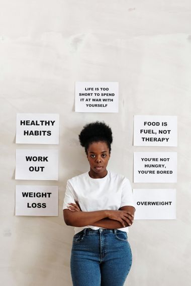Person standing with crossed arms beside signs reading healthy habits, work out, weight loss, food is fuel, not therapy, and overweight.