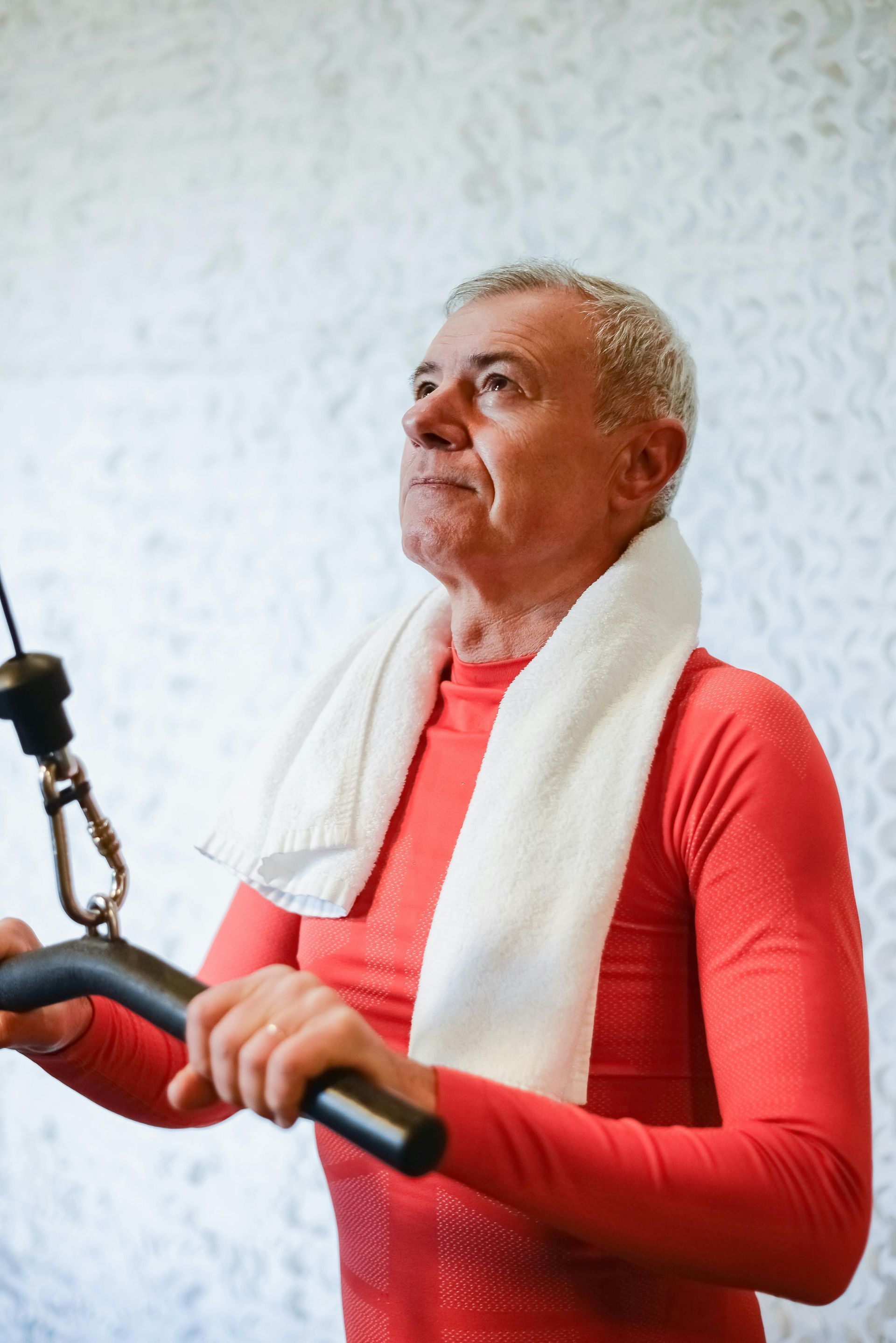 Man in red shirt with white towel around neck using exercise machine, looking upward