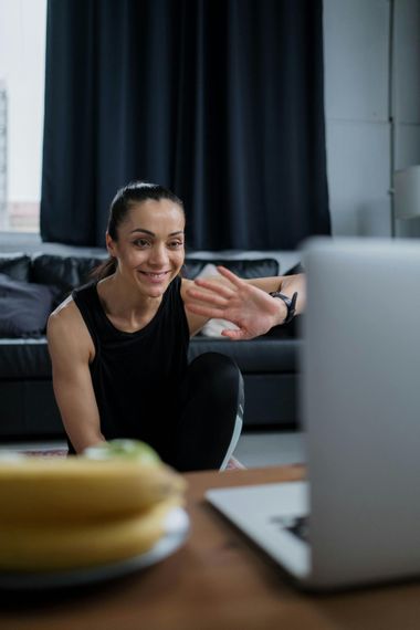 Woman waving during a video call from her couch beside a laptop