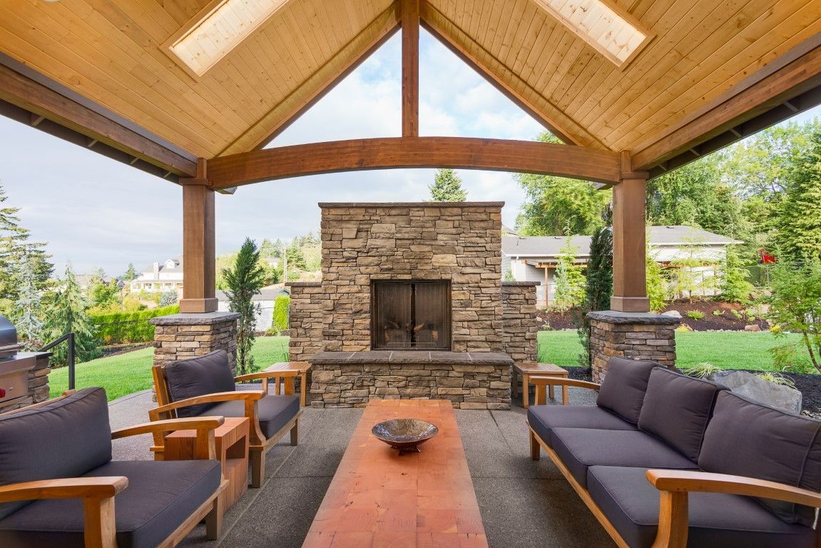Covered outdoor patio with stone fireplace, wood ceiling, and dark cushioned seating.