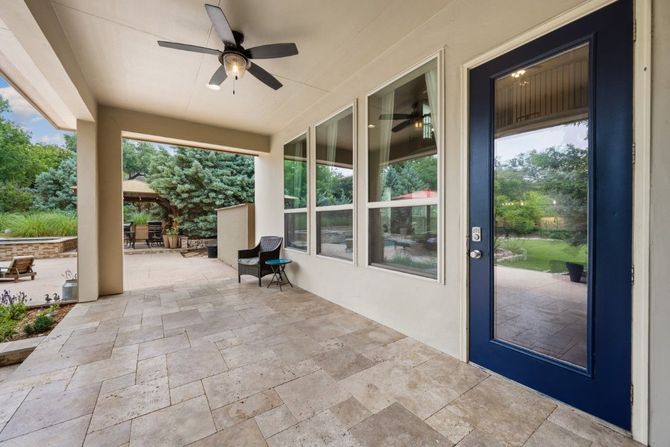 Covered patio with stone floor, ceiling fan, blue door, and windows overlooking a garden.