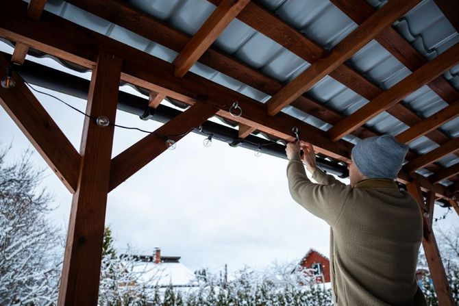 Person on a ladder fastening a wooden roof frame outdoors in winter.