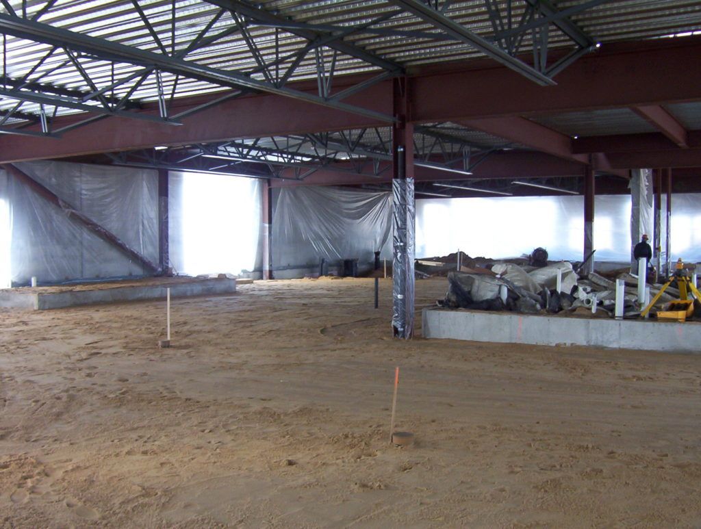 Indoor construction site with dirt floor, steel beams, and covered materials along the right wall