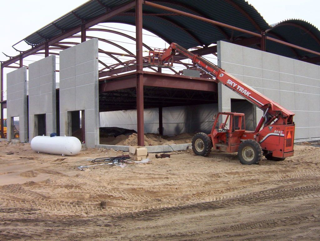 Partially built metal barn with a red telescopic loader on muddy ground