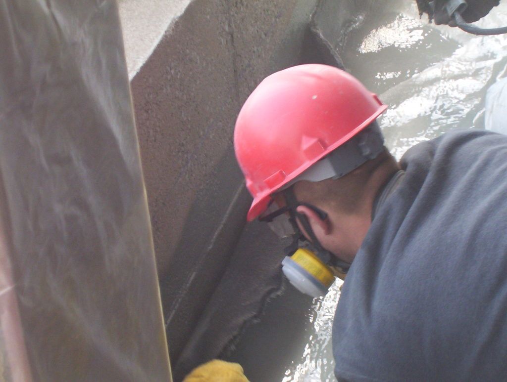 Worker in a red hard hat inspecting wet concrete in a narrow construction area