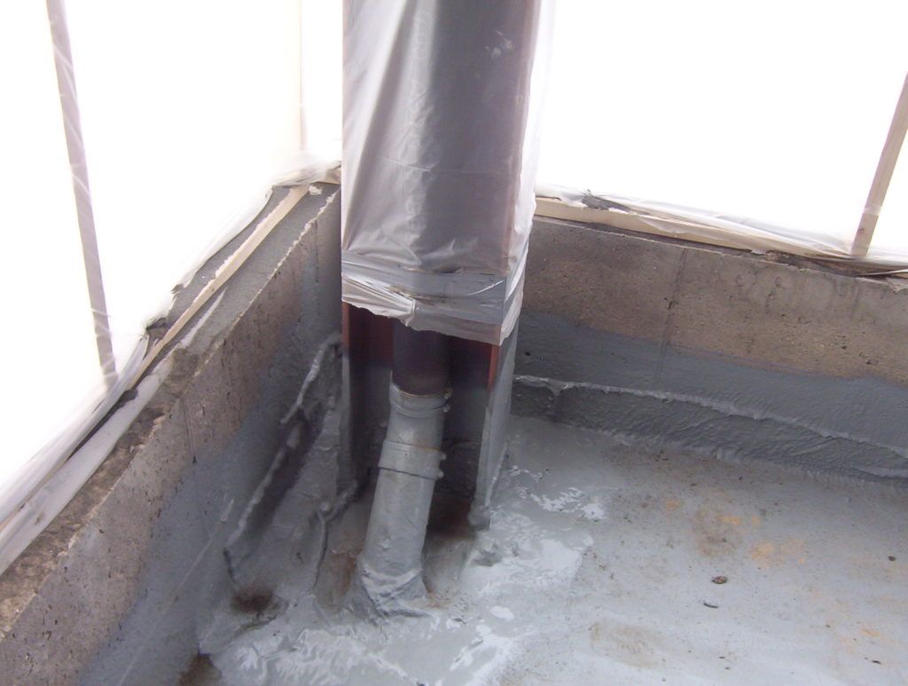 Corner of a rooftop with a gray vent pipe and metal flashing on a concrete surface.