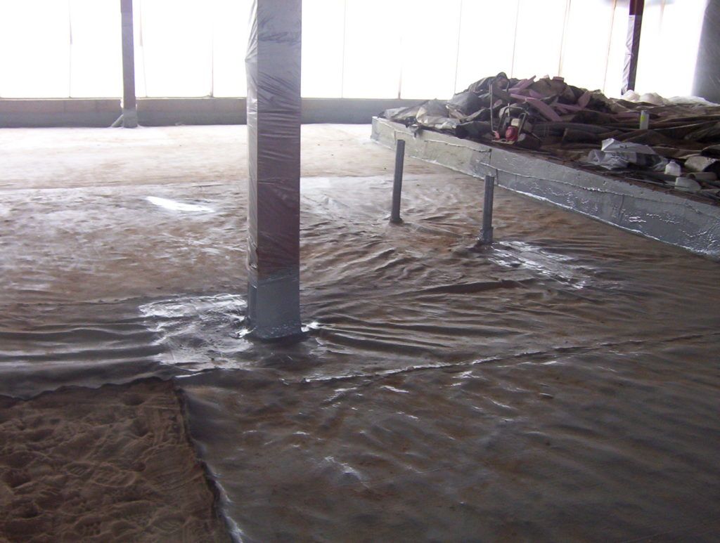 Floodwater inside a building with a central pillar and debris piled on a raised platform.
