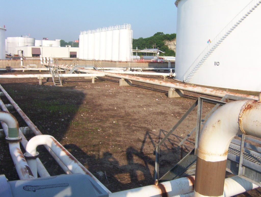 Industrial site with white storage tanks and pipes over a dirt area on a clear day