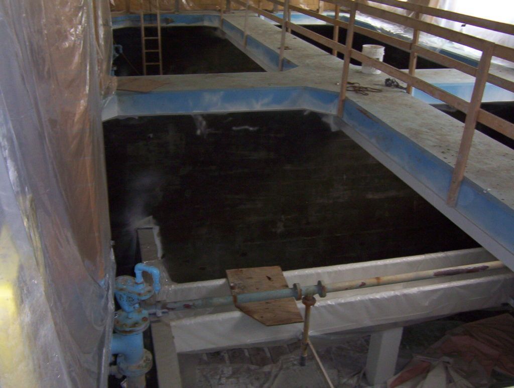 Industrial tank with dark liquid, blue railings, and a metal walkway.