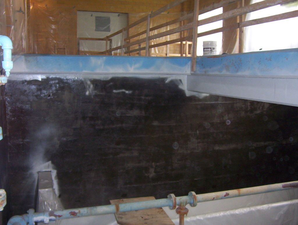 Large black tank or pond interior with water, blue rim, and pipes in an indoor industrial setting