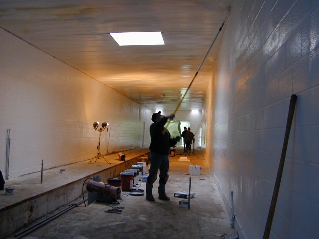 Workers in a white hallway tunnel, installing or repairing the interior walls and ceiling.