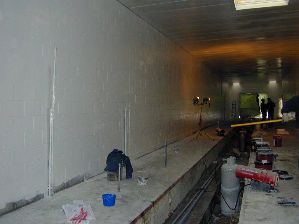 Long, dim tunnel with workers and equipment along a raised concrete ledge