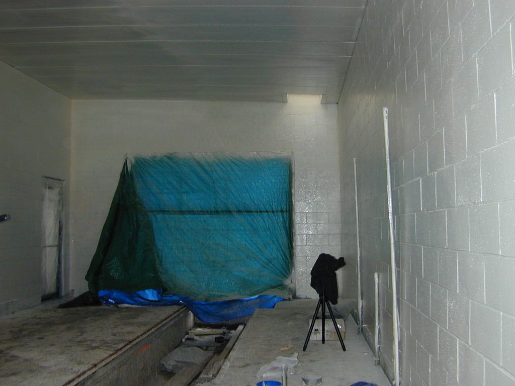Empty tiled room with a tarp-covered pile and a tripod on the floor