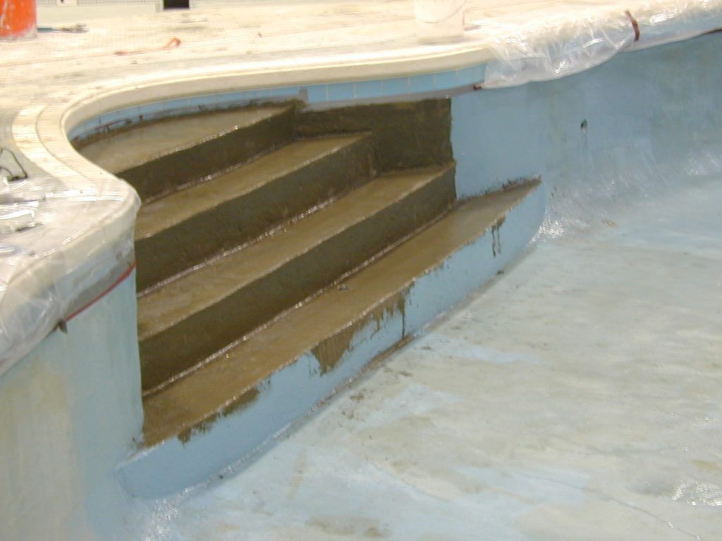 Empty drained swimming pool with steps and cracked blue interior lining