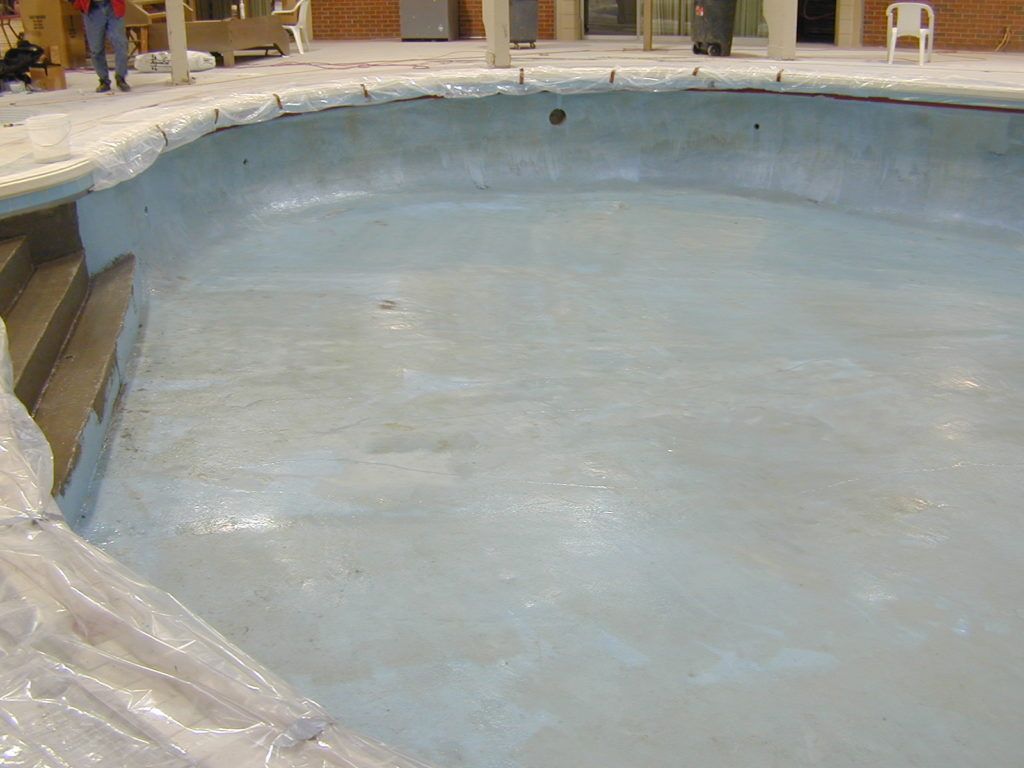Empty drained swimming pool with pale blue interior and plastic sheeting along the edge