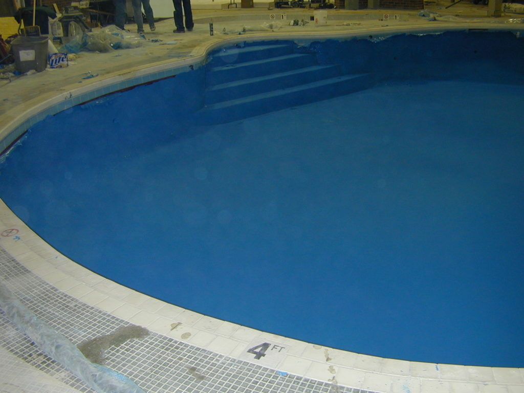 Empty blue swimming pool with a curved white tiled edge indoors.