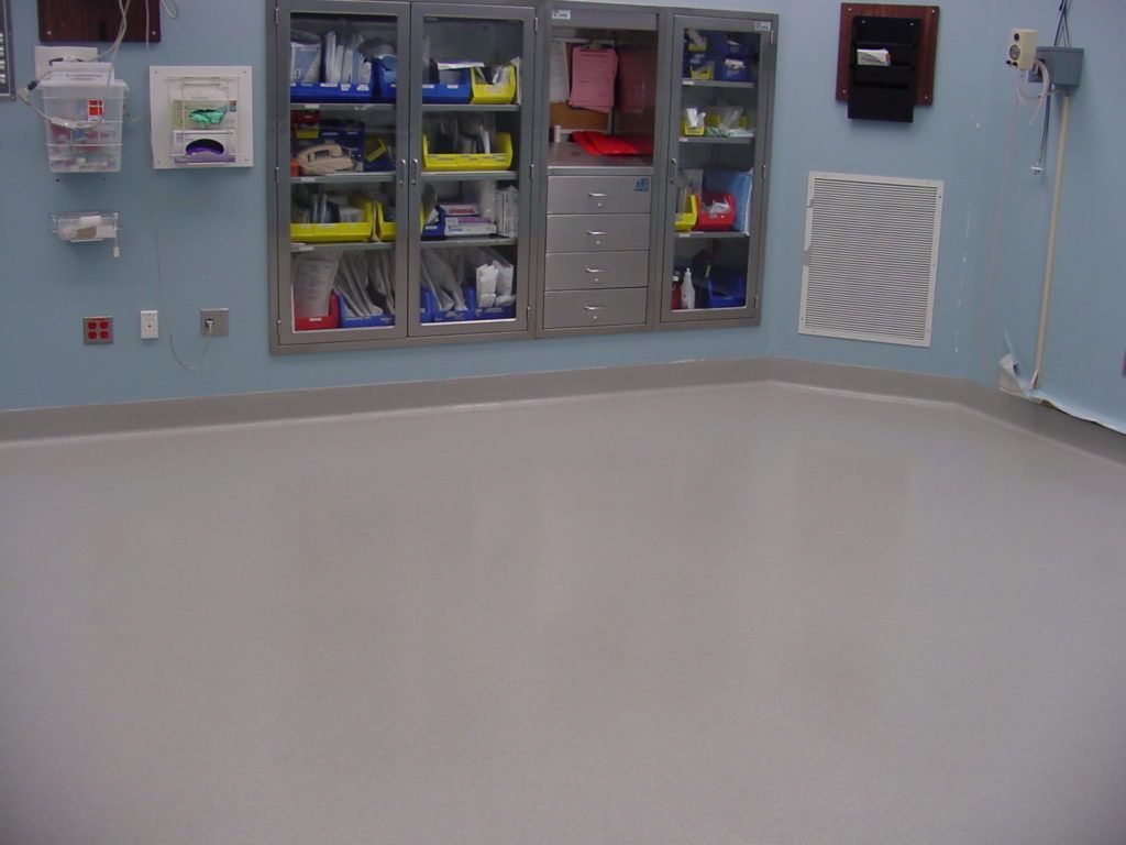 Empty hospital room with blue walls, built-in supply cabinets, and a clean gray floor