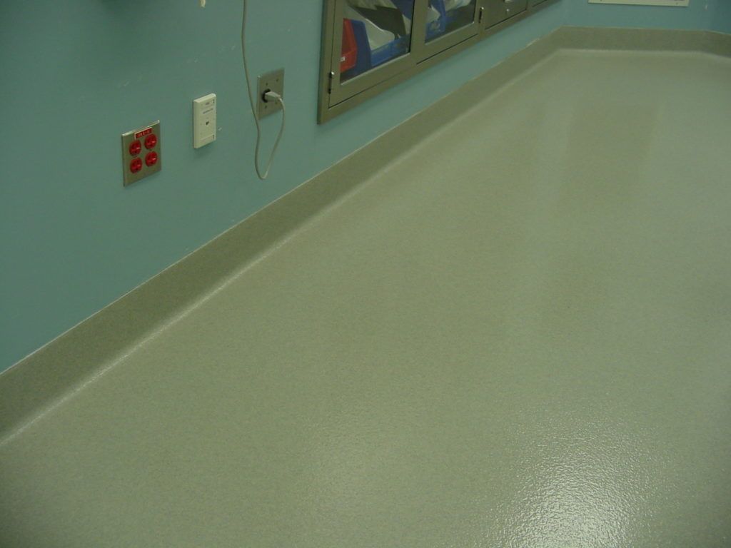 Empty hospital room corner with pale green floor, blue wall, and outlets near a window.