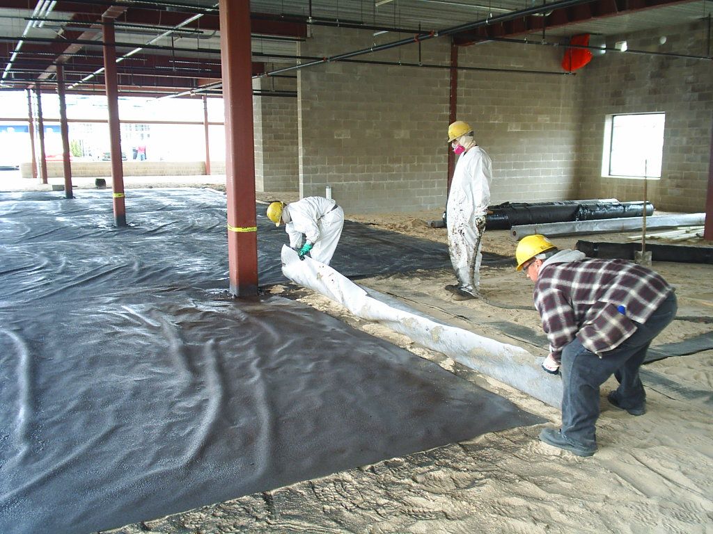 Workers in hard hats spreading plastic sheeting inside an unfinished building.