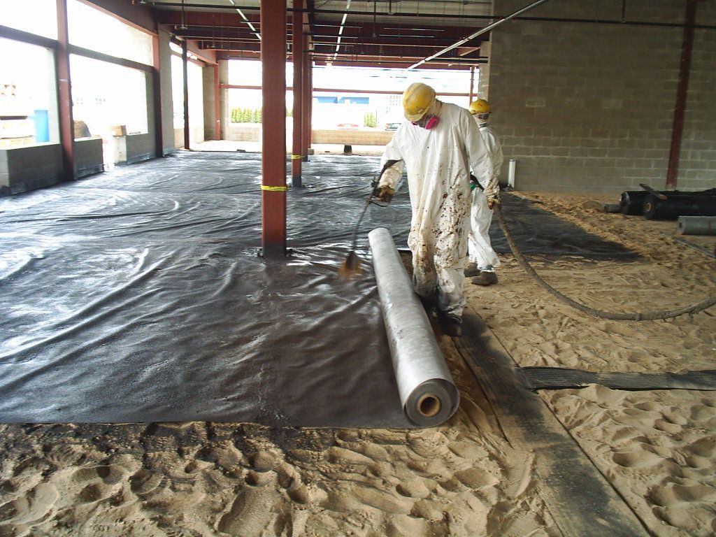 Worker installing black floor liner in unfinished building interior
