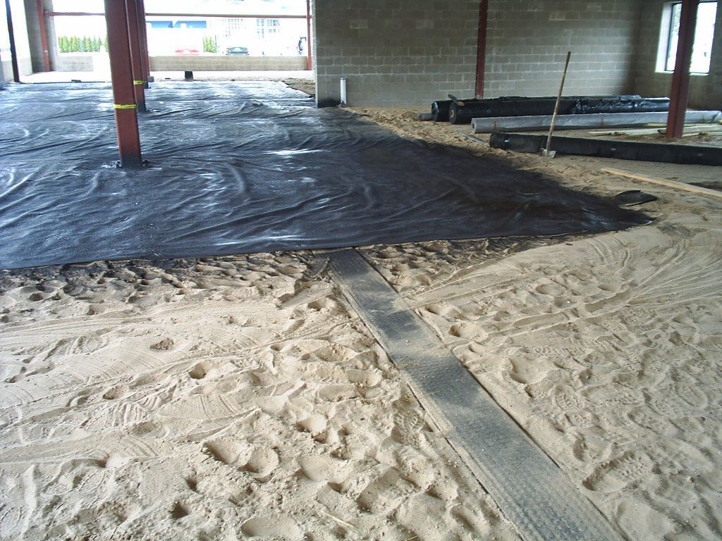 Construction site floor with sand and black plastic sheeting under a building frame
