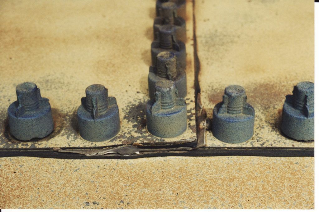 Row of weathered metal bolts and nuts on a rust-stained industrial surface