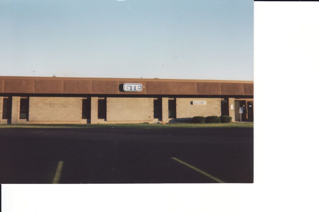 Low tan brick storefront with a brown roof and parking lot in front under a clear sky