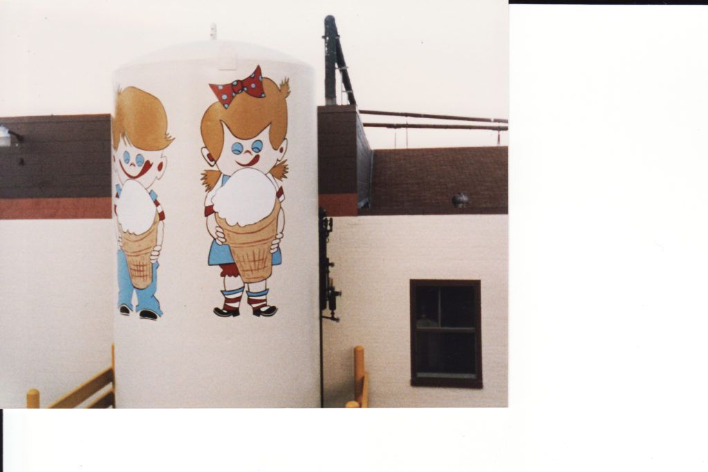 Two cartoon children painted on a white wall beside a dark window and brown building exterior